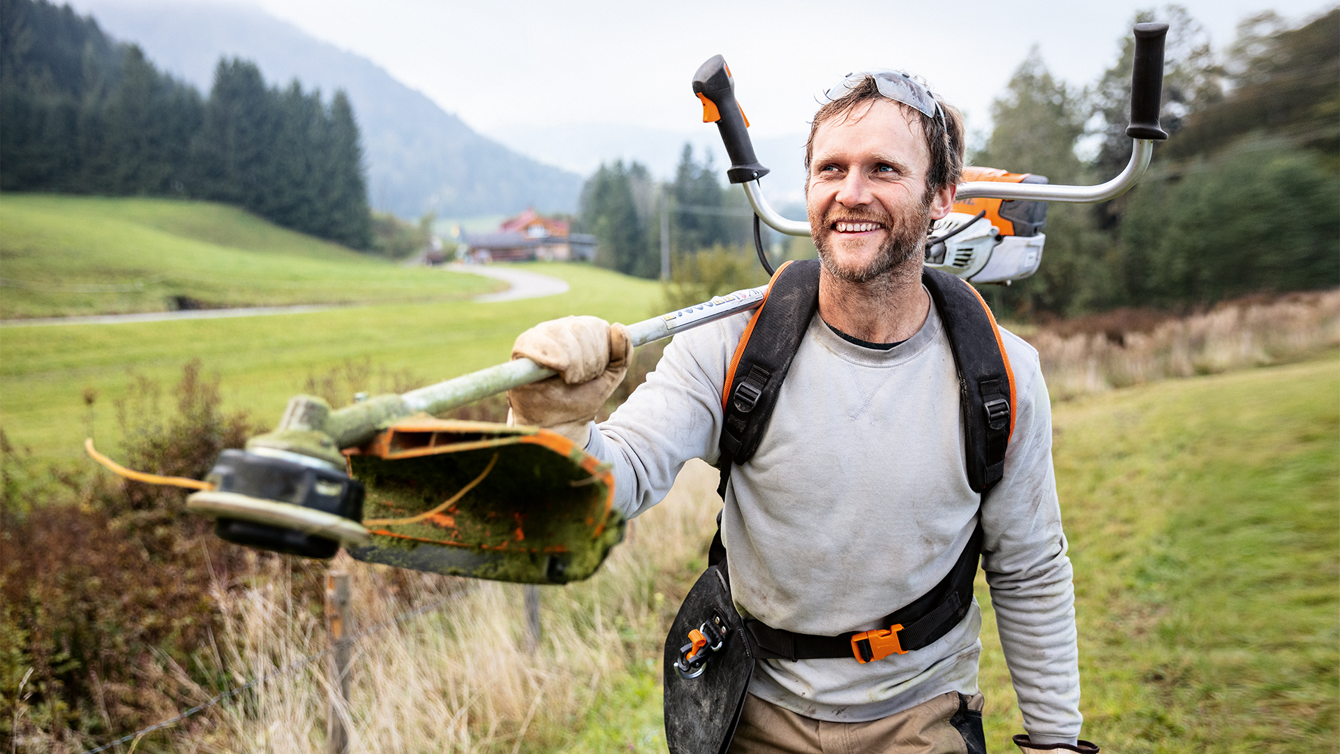 Mann med STIHL trimmer og Advance PLUS universalbæresele på en eng