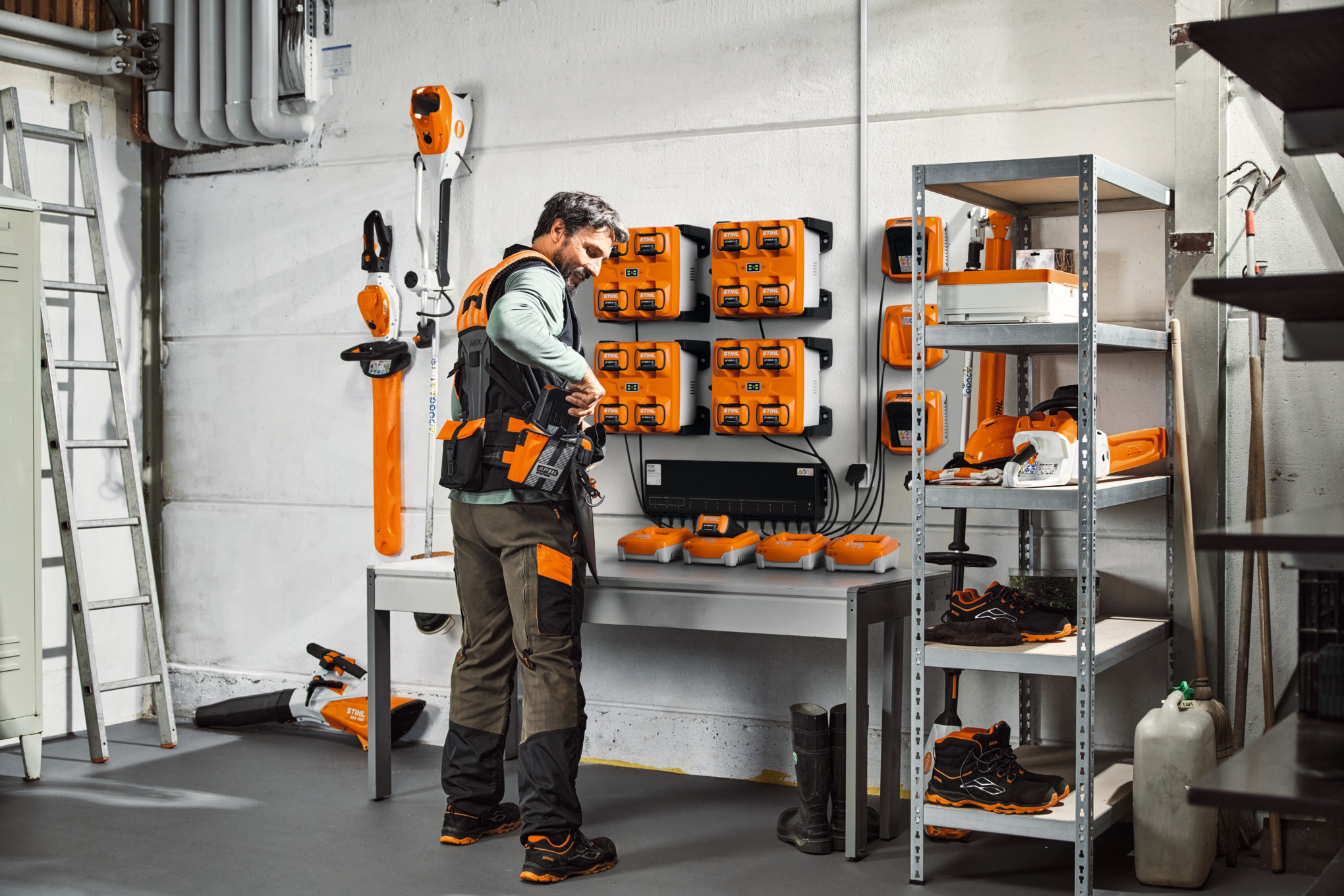 En mann i et lagerrom med STIHL-enheter og batterier bærer STIHL ADVANCE X-Flex modulære beltesystem