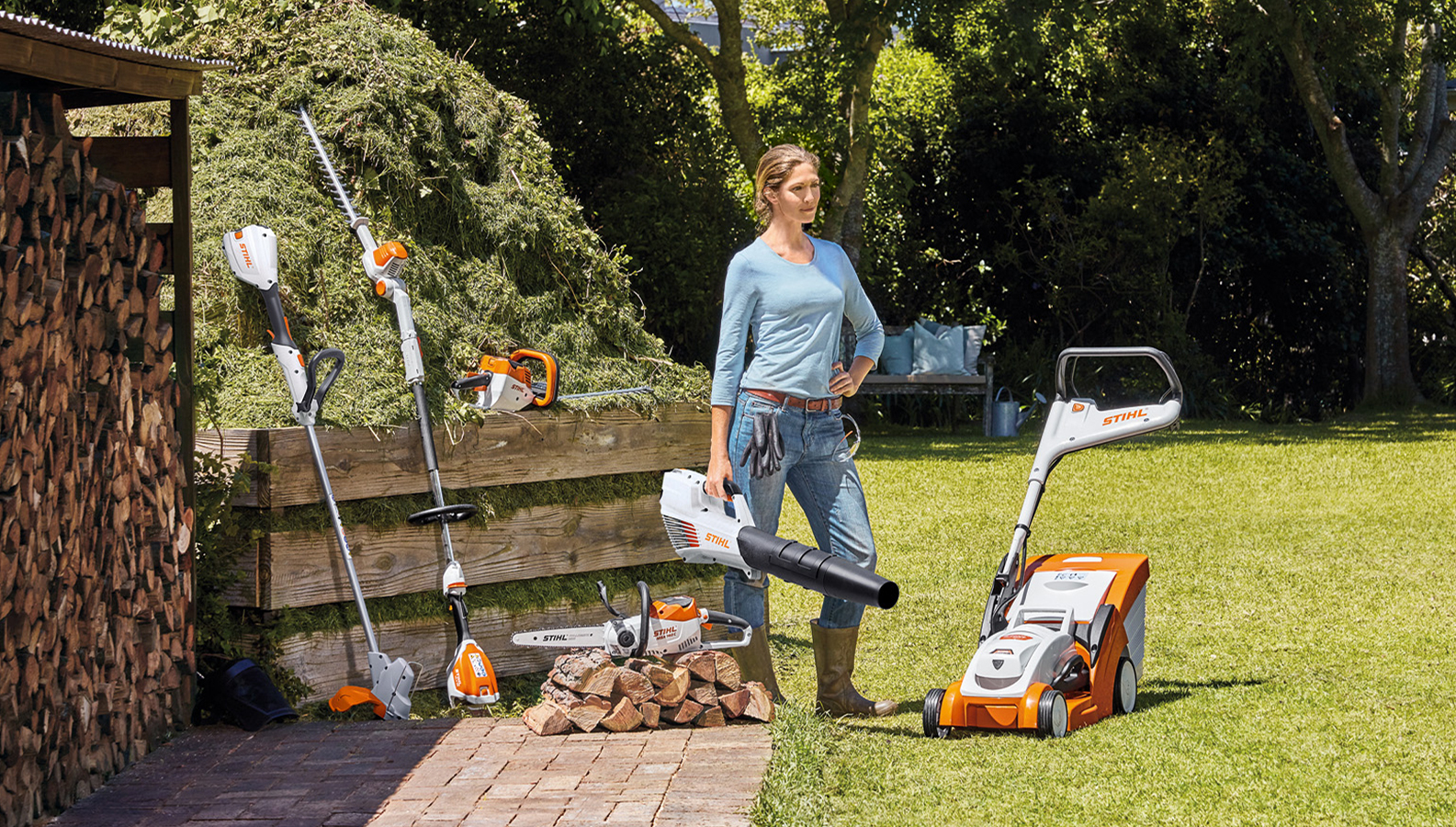 Kvinne som står i hagen med et utvalg batteriprodukter fra STIHL