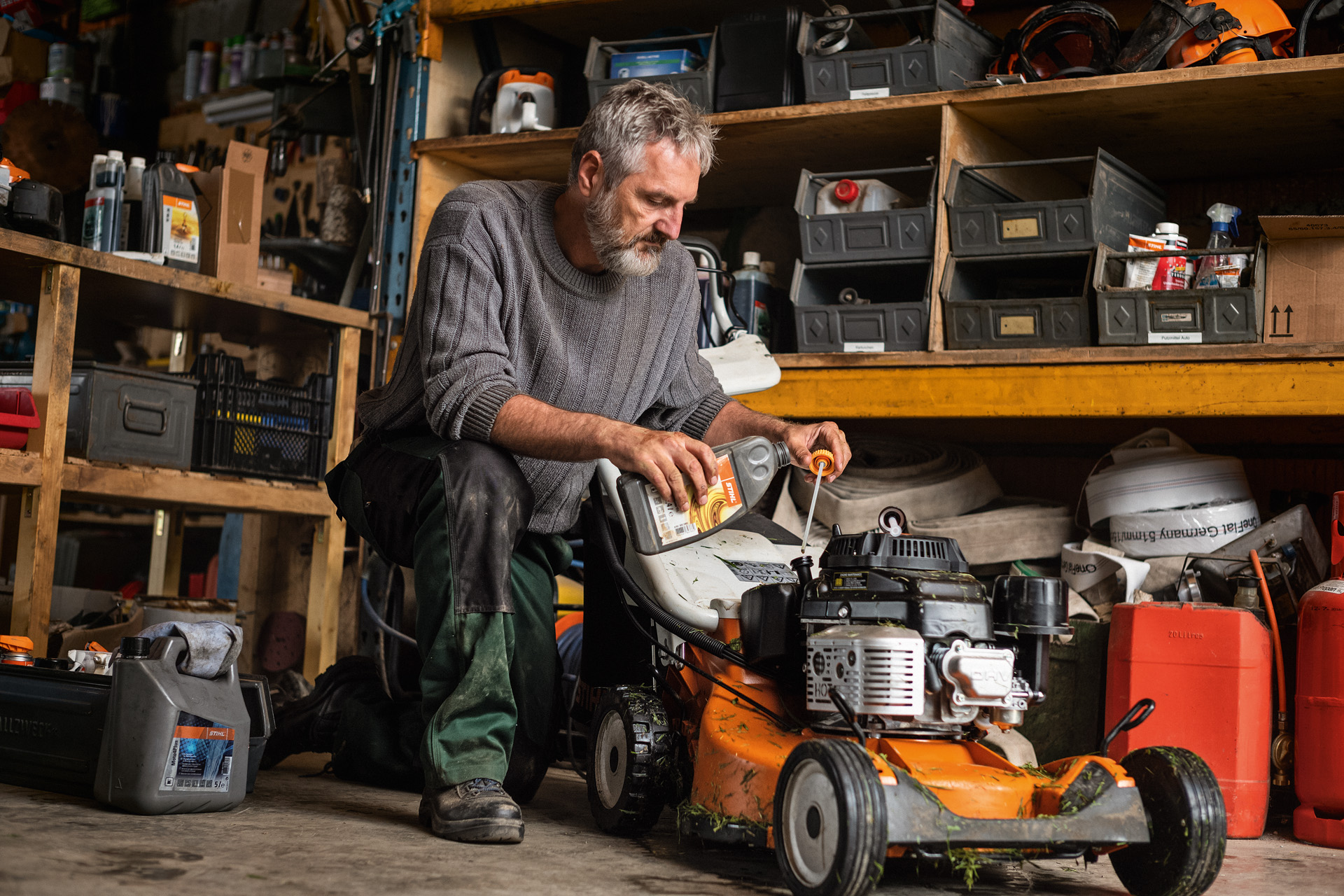 En mann utfører vedlikehold på en bensindrevet gressklipper av type STIHL RM 756 i en garasje