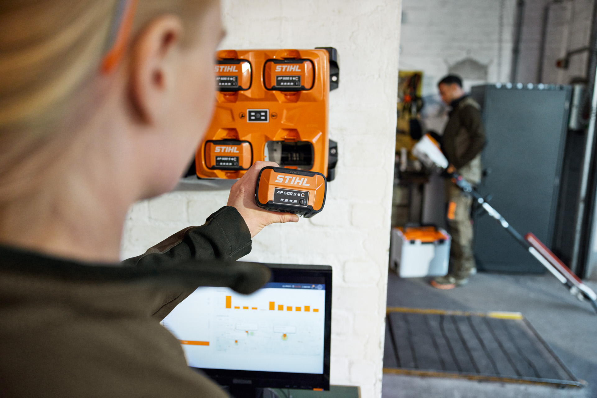 En kvinne foran en bærbar PC tar en AP 300 S ut av en STIHL AL 301-4 multilader