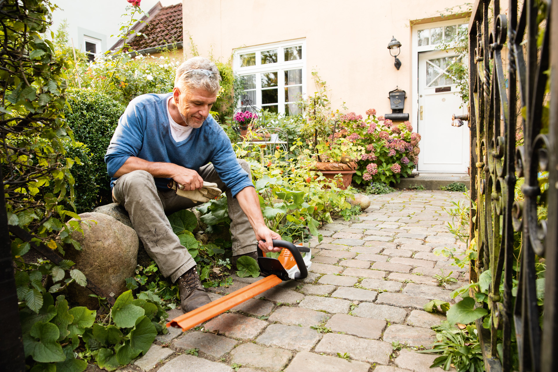 En mann med en STIHL HSA 45 elektrisk hekksaks i AI-serien foran et hus