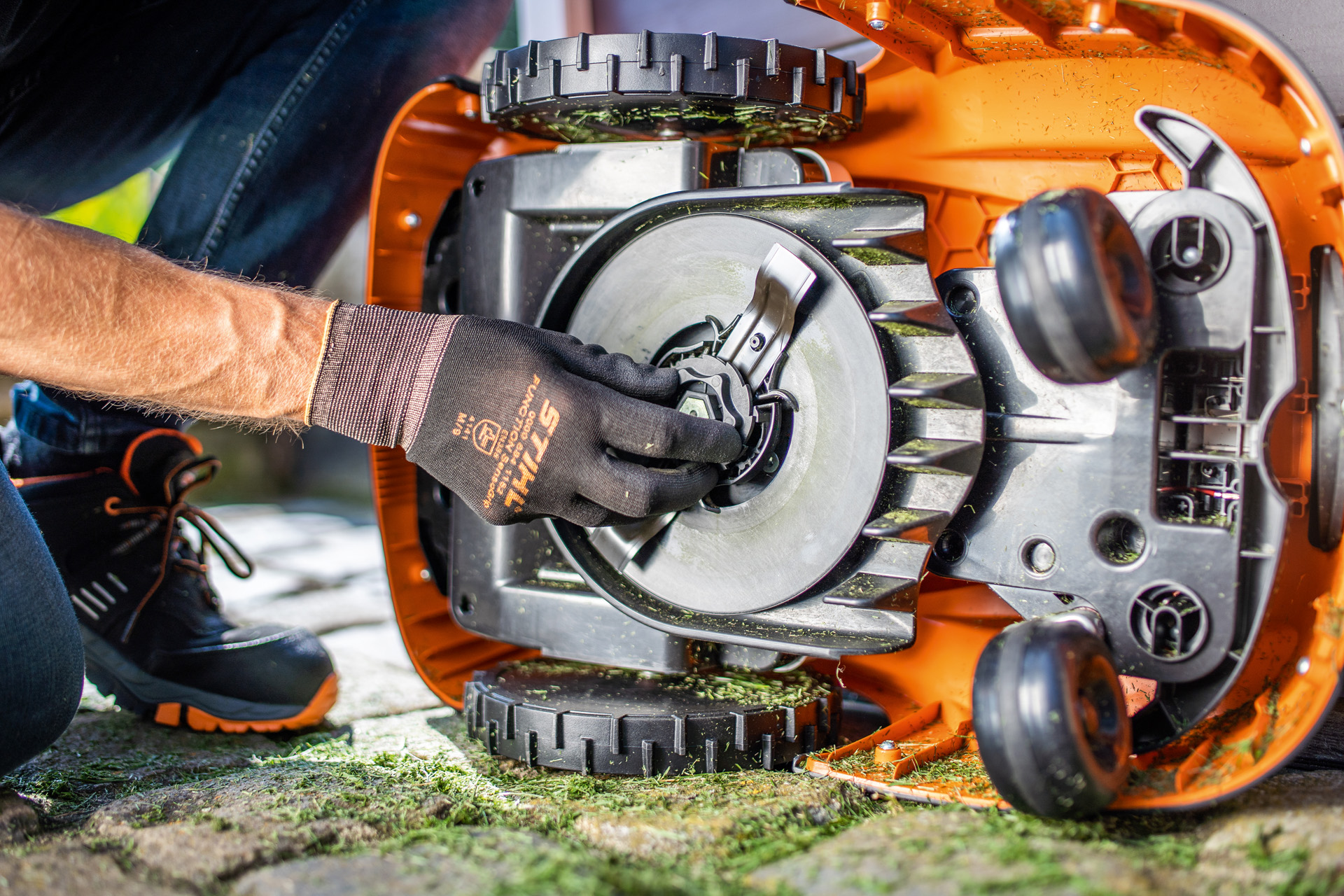 Den rene undersiden av en STIHL iMOW® robotgressklipper, der en person med hansker undersøker bladet