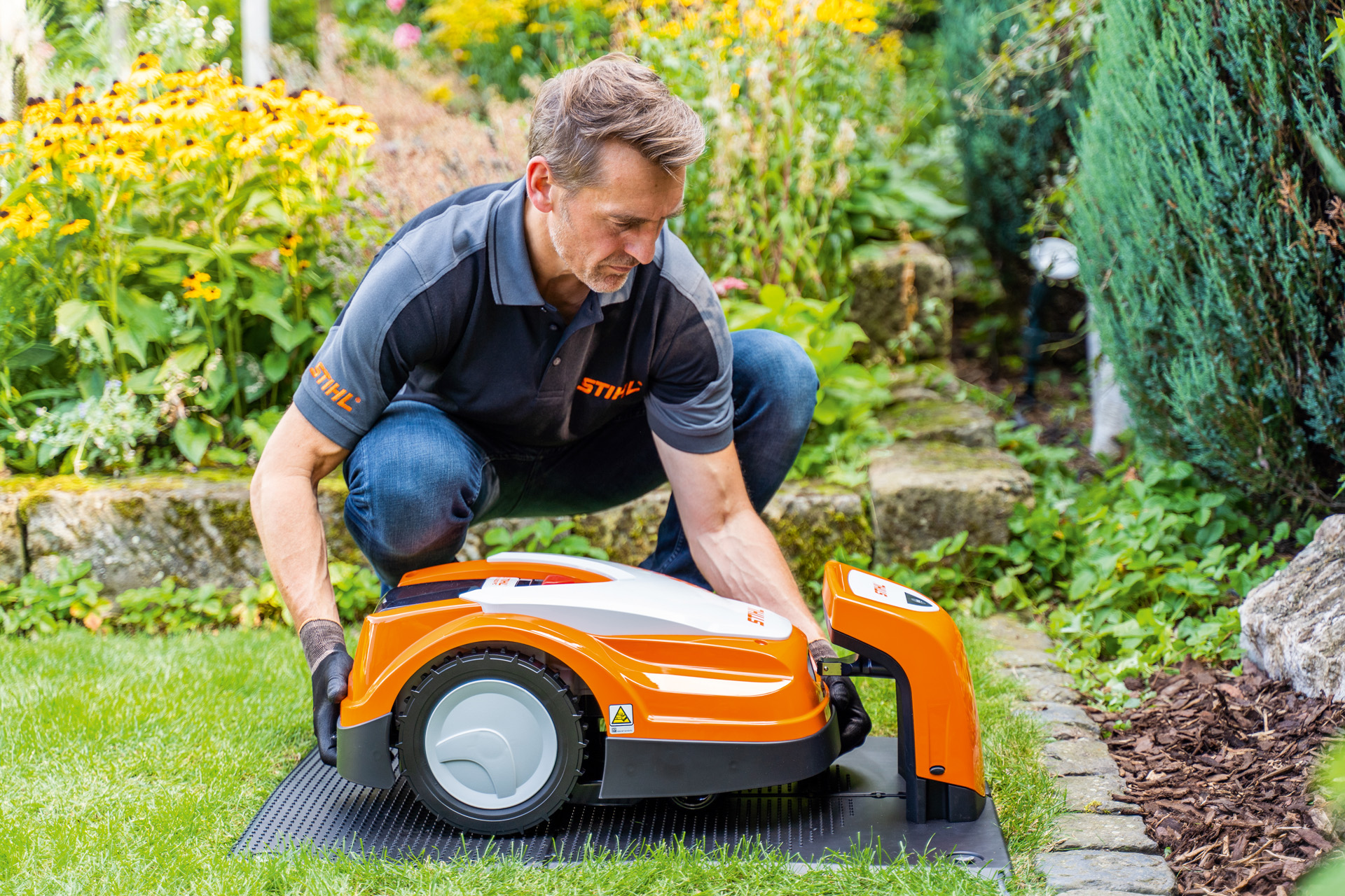 En STIHL-forhandler plasserer en STIHL iMOW robotgressklipper i ladestasjonen i en hage