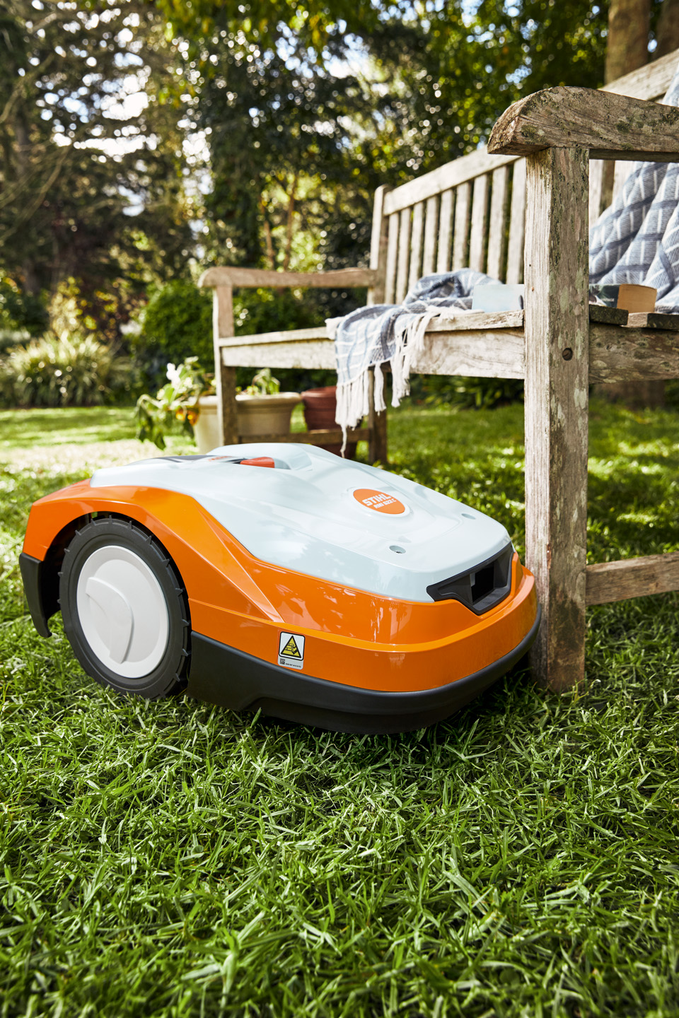 En STIHL iMOW® RM 522 robotgressklipper ved siden av en benk ute på en gressplen