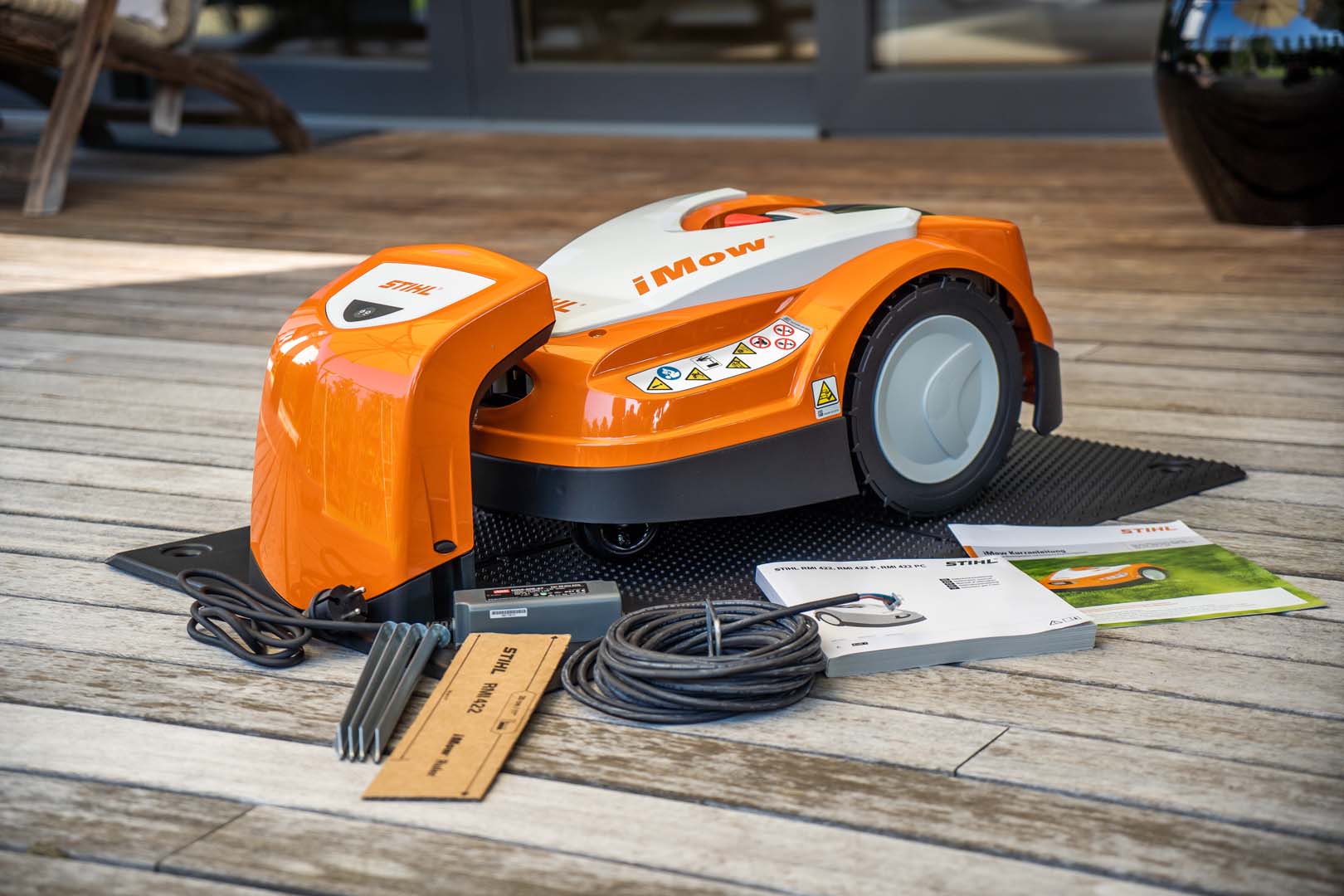 En STIHL iMOW® 422 robotgressklipper på en terrasse med avgrensingstråd og brukerhåndbok