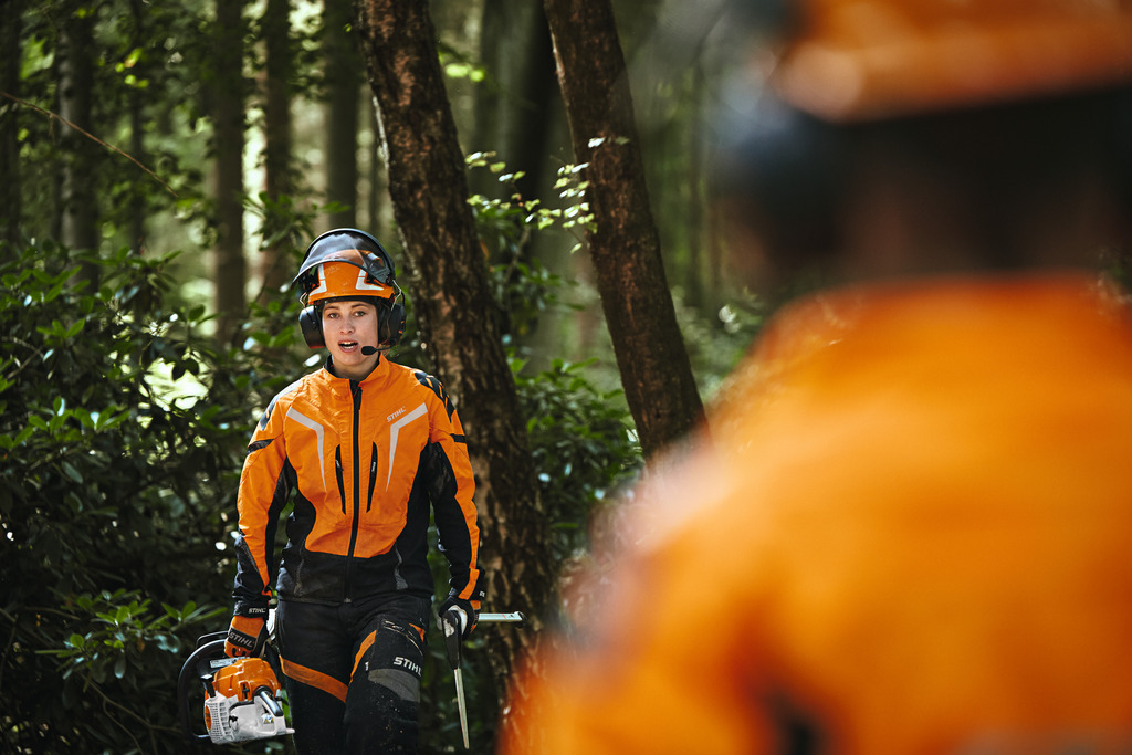 En kvinnelig skogsarbeider går kledd i STIHL arbeidsklær i soloppgang på en høyde