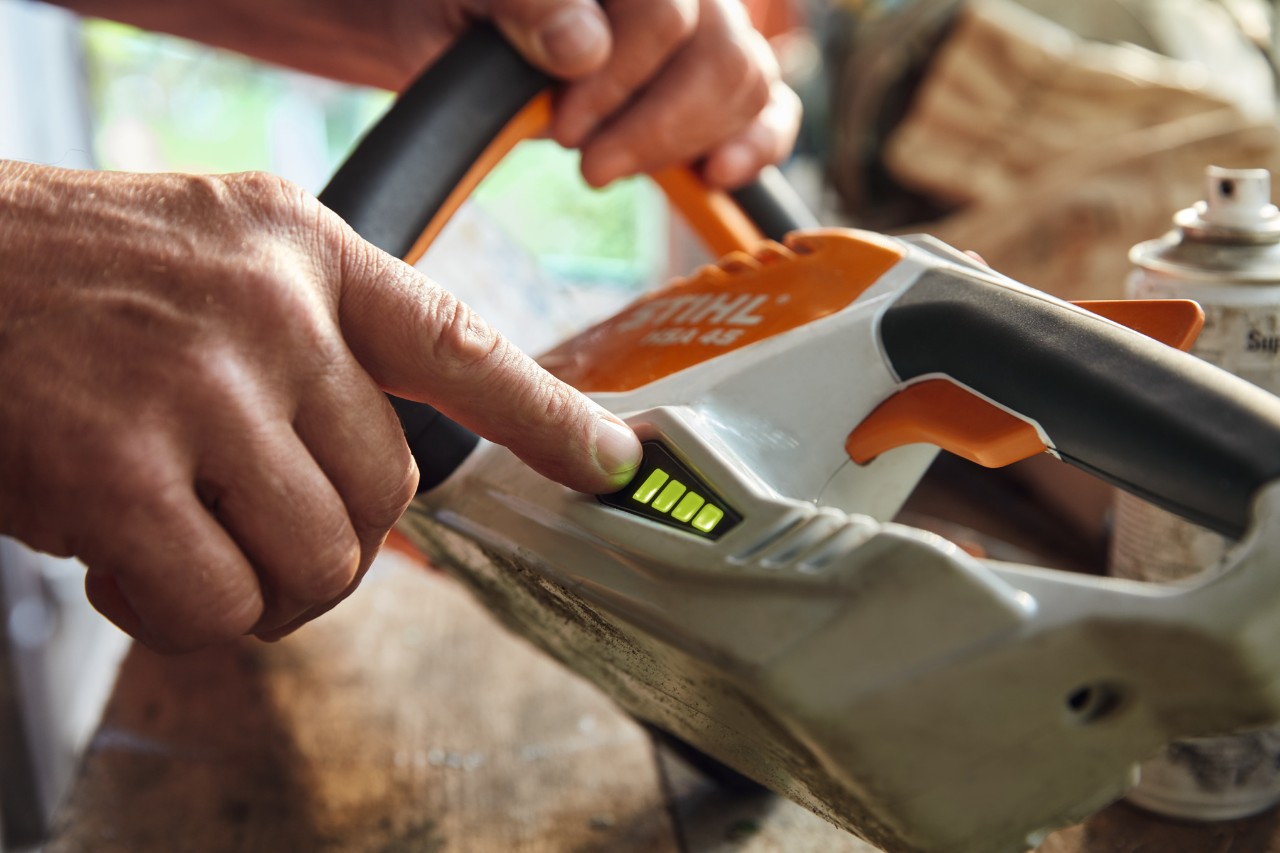 En person sjekker ladestatusen på den batteridrevne hekksaksen STIHL HSA 45.